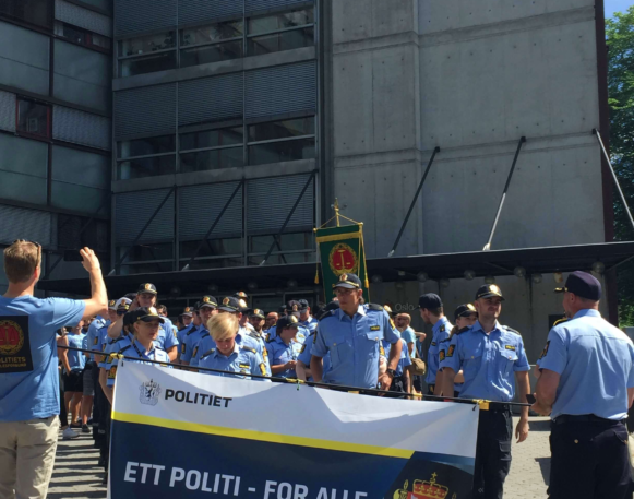 en gruppe politibetjenter står utenfor politihuset med en banner mellom seg, med tekste ett politi - for alle